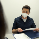 A man wearing an N95 mask interviews a potential job candidate across a desk at the Focus office.